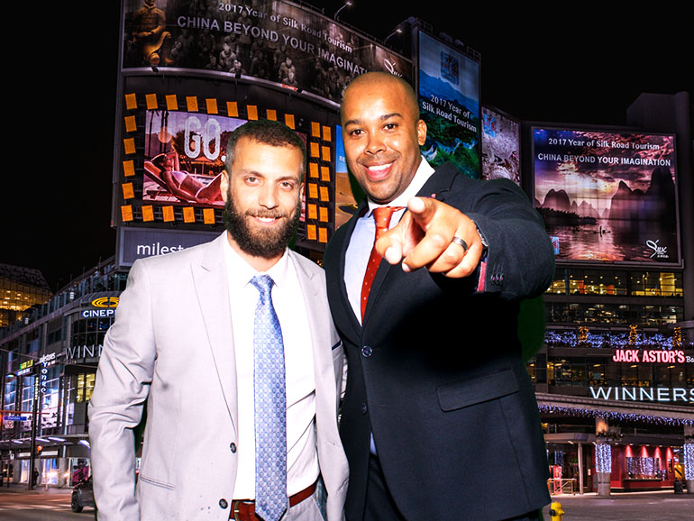 Two men stand in front of a green-screen image of Dundas Square in Toronto at a corporate event where they rented a photo booth.