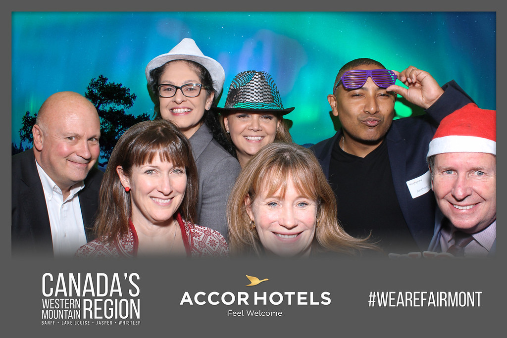 A group of guests wearing fun props smiling for a custom branded green screen photo booth at a Fairmont corporate event, featuring a digital Northern Lights backdrop and a WEAREFAIRMONT branding overlay