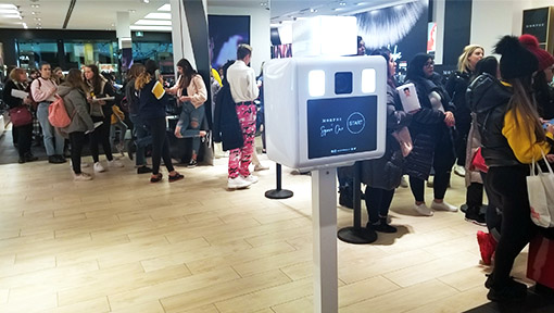 A modern white custom branded photo booth stationed at a MORPHE retail store, featuring a custom digital screen and a long line of guests waiting to engage during a corporate brand activation in the GTA.