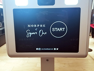 close-up view of a custom branded photo booth touch screen for a MORPHE corporate brand activation, featuring a sleek black background, white branding text, and a circular start button.